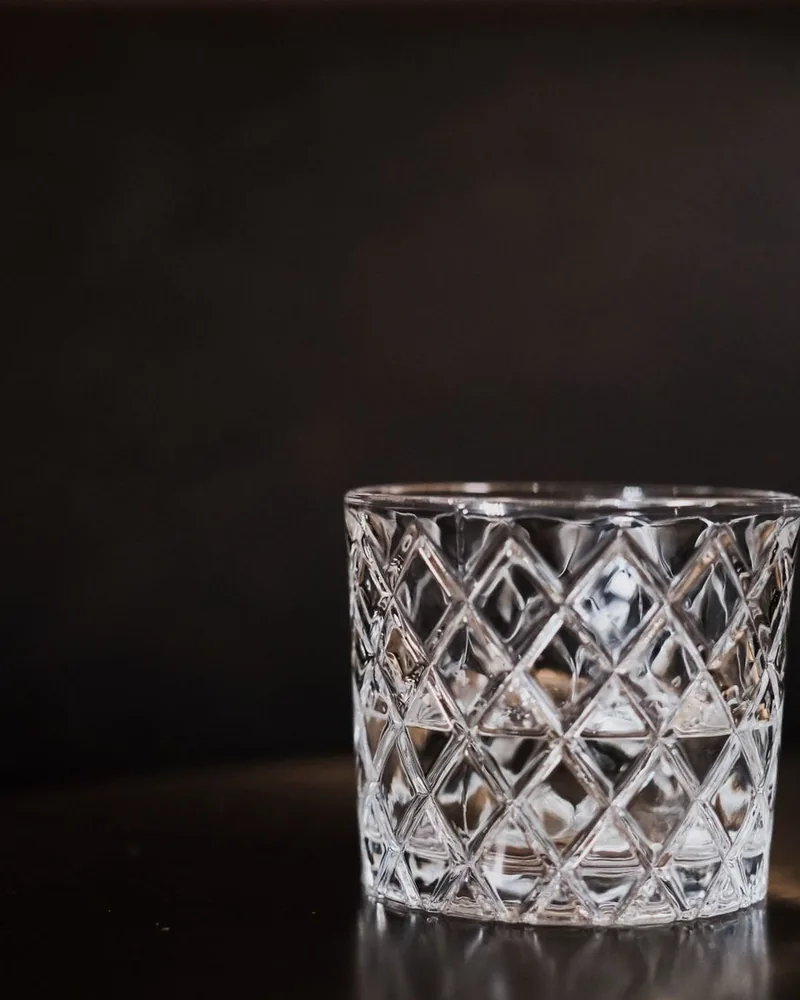 Vaso de cristal con retícula de rombos tallada, sobre una mesa oscura atravesada por un haz de luz