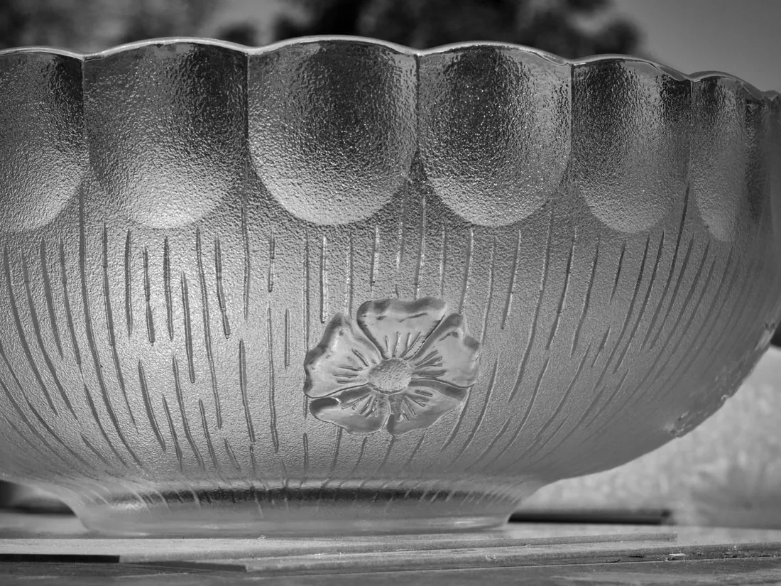 Cuenco de vidrio con superficie satinada, estrías finas y un motivo floral en relieve, iluminado de lado